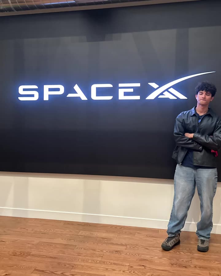Deon standing in front of the illuminated SpaceX logo wall
